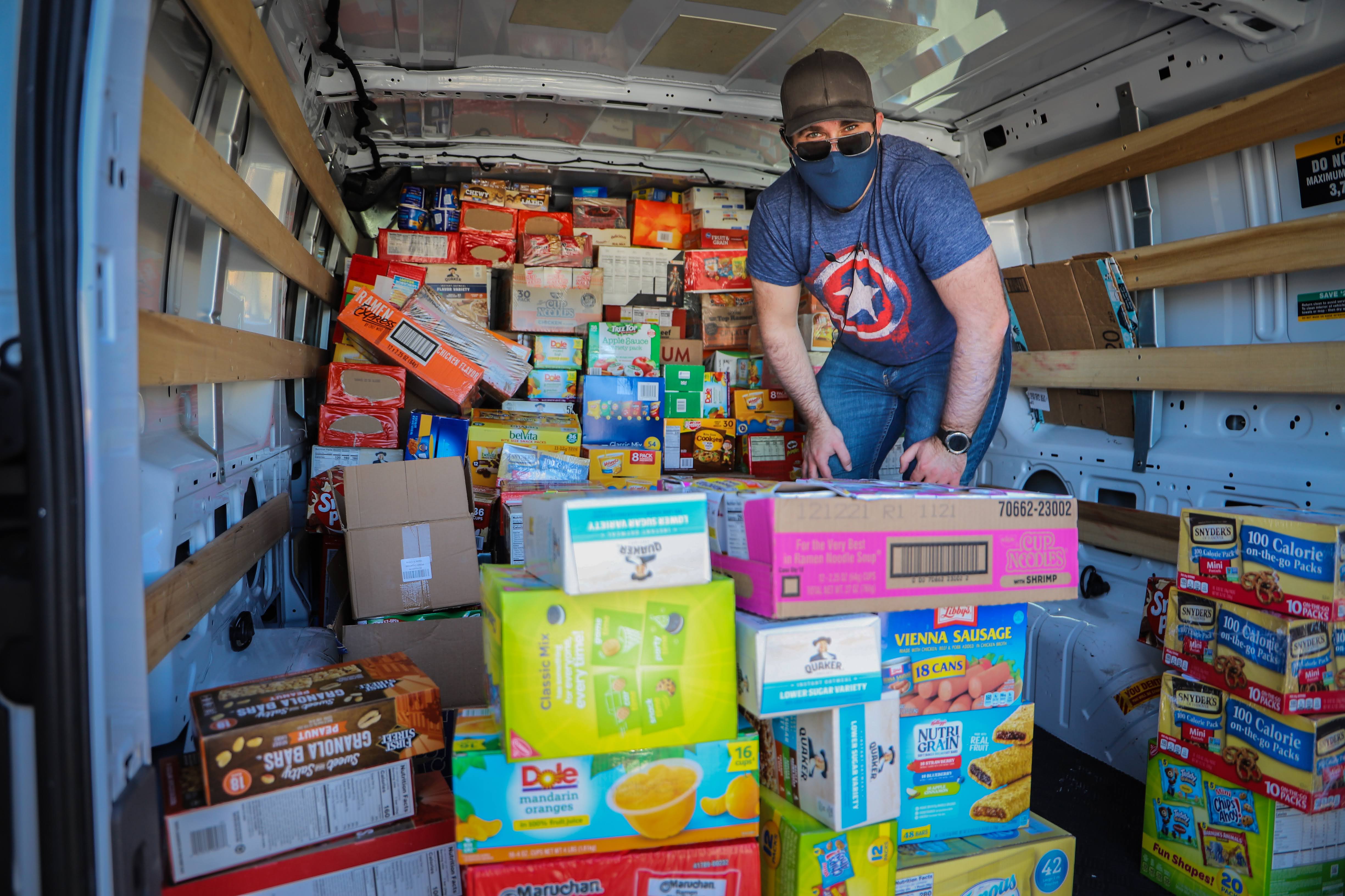 Brett Haddoak, wearing a cap and face mask, stacking boxes of packaged food inside a fully loaded cargo van.